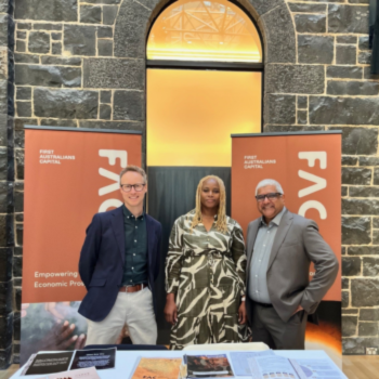 Three people standing at a First Australians Capital information stand at an event.